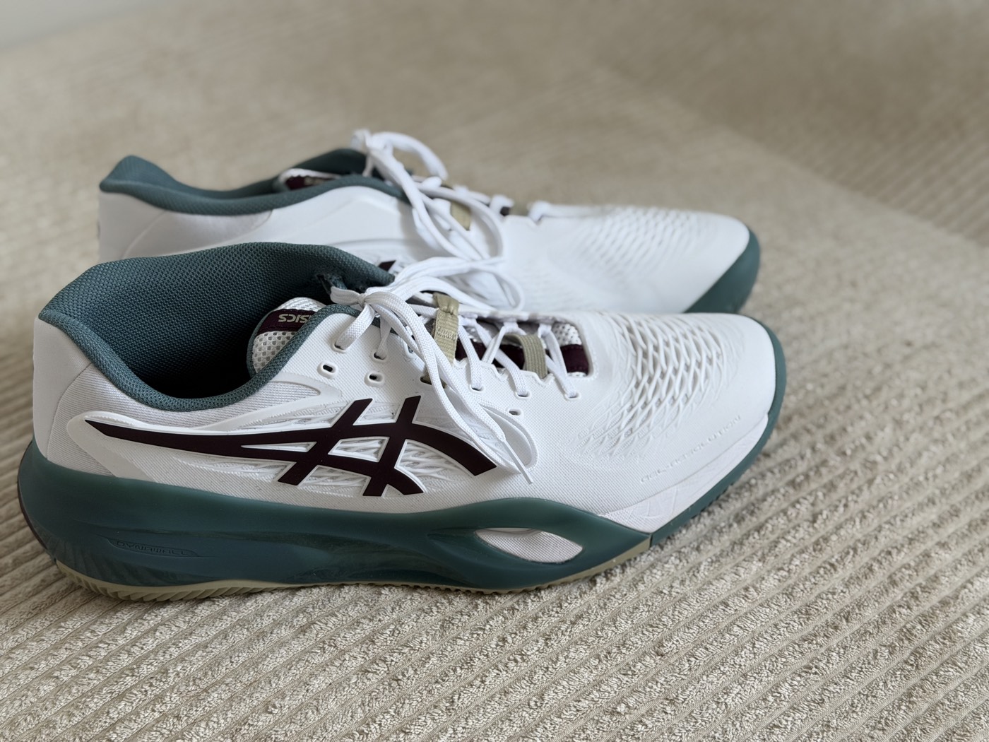 Beide Schuhe von der Seite: weißes Obermaterial, tiefgrüne Sohle und Kragen, dunkelroter ASICS-Streifen